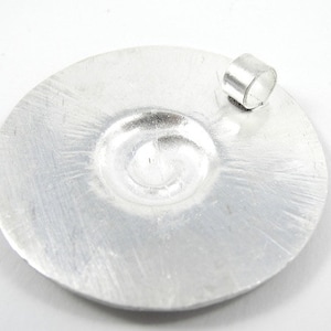 May include: A silver circular pendant with a swirl design and a jump ring for attaching a chain.