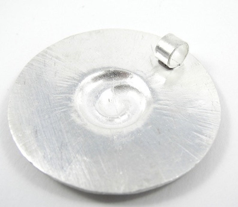 May include: A silver circular pendant with a swirl design and a jump ring for attaching a chain.