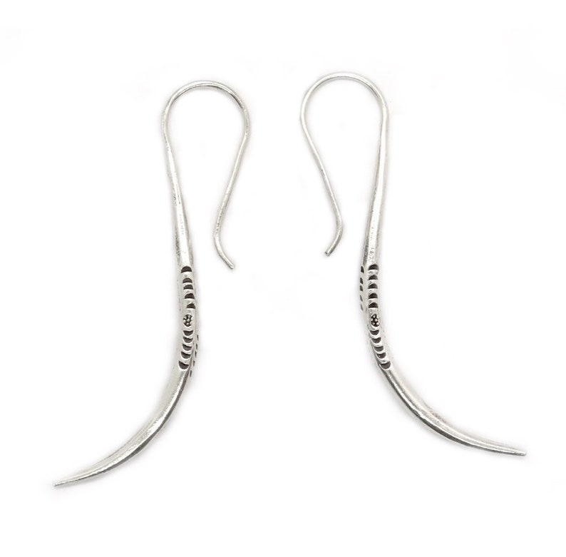 May include: A pair of silver dangle earrings with a curved design and a textured pattern. The earrings have a hook closure.