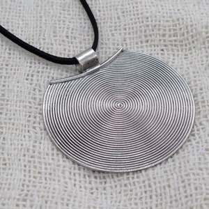 May include: A silver pendant necklace with a circular pendant featuring a concentric circle design. The pendant is attached to a black cord.