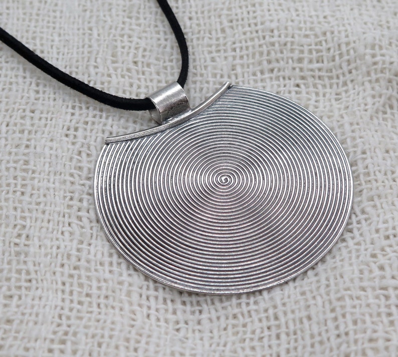 May include: A silver pendant necklace with a circular pendant featuring a concentric circle design. The pendant is attached to a black cord.