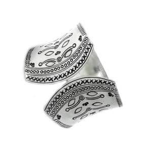 Puede incluir: Una pulsera de pu&ntilde;o plateada con un dise&ntilde;o abierto. La pulsera presenta intrincados patrones negros grabados, que incluyen formas geom&eacute;tricas y l&iacute;neas. El dise&ntilde;o se envuelve alrededor de la mu&ntilde;eca, creando un accesorio audaz y elegante.