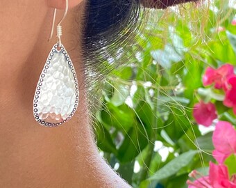 May include: Silver teardrop earrings with a hammered texture and a beaded border.