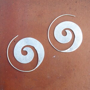 May include: A pair of silver spiral hoop earrings. The earrings are made of a thin metal and have a simple, elegant design.