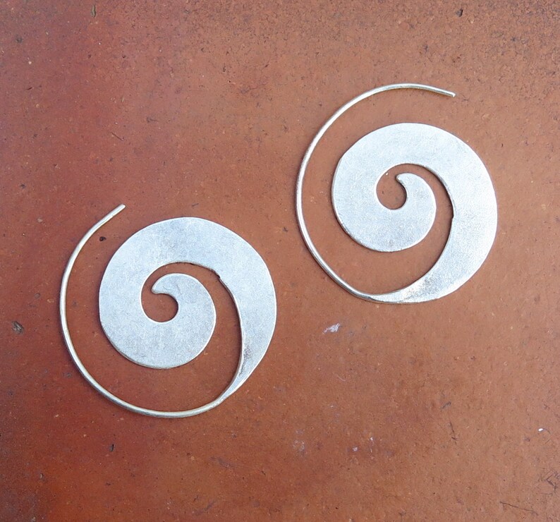 May include: A pair of silver spiral hoop earrings. The earrings are made of a thin metal and have a simple, elegant design.