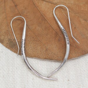May include: A pair of silver hoop earrings with a textured design. The earrings are curved and have a hook closure.