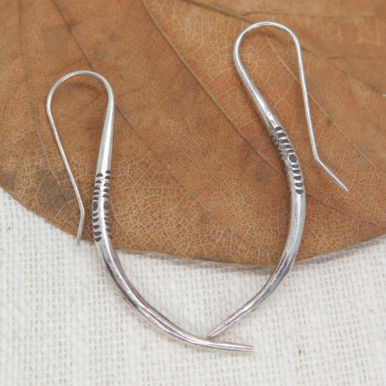 May include: A pair of silver hoop earrings with a textured design. The earrings are curved and have a hook closure.