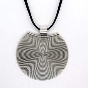 May include: A silver pendant necklace with a circular pendant featuring a concentric circle design. The pendant is attached to a black suede cord.