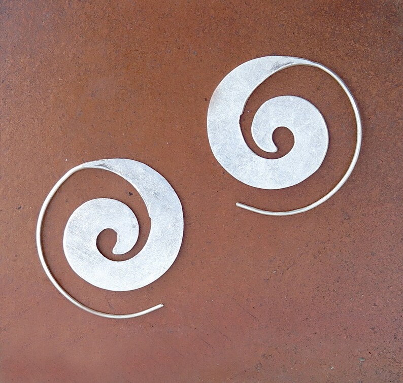 May include: A pair of silver hoop earrings with a spiral design. The earrings are made of metal and have a simple, elegant look.