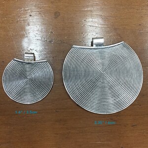 May include: Two silver metal pendants with a spiral design. The smaller pendant measures 1.4 inches or 3.5 cm in diameter. The larger pendant measures 2.35 inches or 6 cm in diameter.