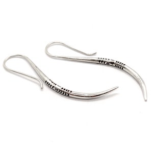 May include: A pair of silver earrings with a curved, pointed design. The earrings have a delicate, intricate pattern etched into the metal.