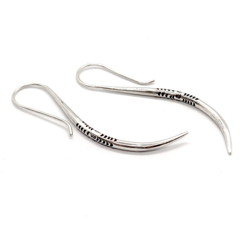 May include: A pair of silver earrings with a curved, pointed design. The earrings have a delicate, intricate pattern etched into the metal.