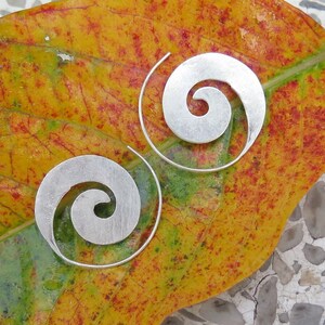 May include: A pair of silver spiral earrings on a yellow and green leaf. The earrings are made of a thin metal and have a simple design.