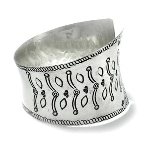 Puede incluir: Pulsera ancha de plata con textura martillada y un patr&oacute;n decorativo negro. La pulsera presenta un dise&ntilde;o curvo y un borde detallado, con un estilo abierto y envolvente.