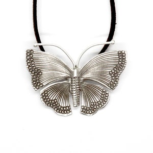 May include: A silver butterfly pendant necklace with a leather cord. The butterfly has a detailed design with textured wings and a beaded edge.
