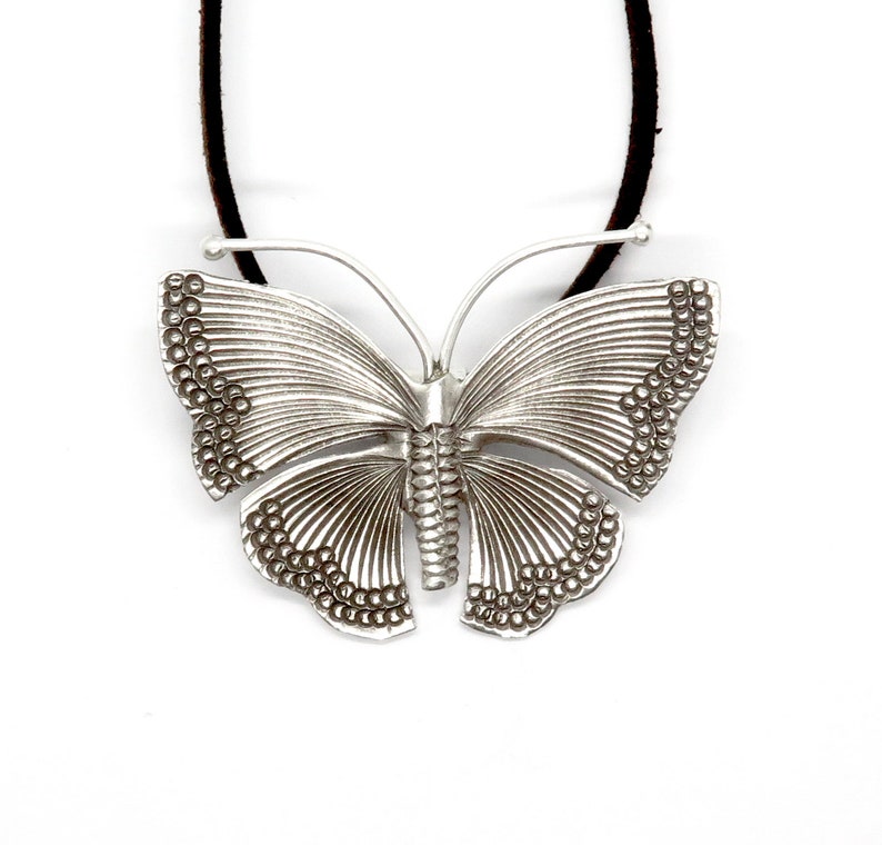 May include: A silver butterfly pendant necklace with a leather cord. The butterfly has a detailed design with textured wings and a beaded edge.
