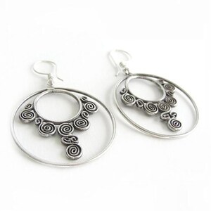 May include: Silver hoop earrings with a detailed spiral design. The earrings have a double hoop design with a dangling spiral pendant.