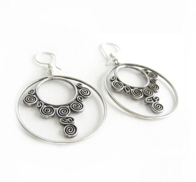 May include: Silver hoop earrings with a detailed spiral design. The earrings have a double hoop design with a dangling spiral pendant.