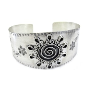 May include: Silver cuff bracelet featuring a spiral sun design and floral accents.