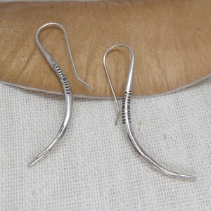 May include: A pair of silver earrings with a curved design and a textured pattern. The earrings are made of metal and have a simple, elegant style.