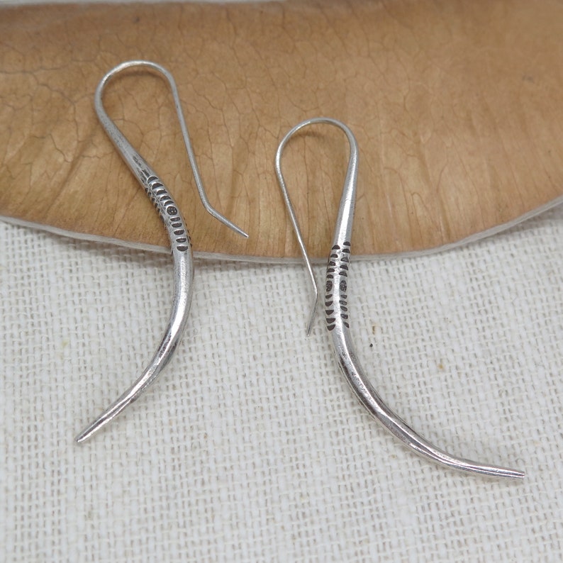 May include: A pair of silver earrings with a curved design and a textured pattern. The earrings are made of metal and have a simple, elegant style.