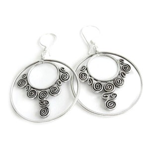 May include: Silver hoop earrings with a decorative design of swirling circles.
