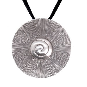 May include: A silver pendant necklace with a circular design featuring a spiral in the centre. The pendant is attached to a black cord.