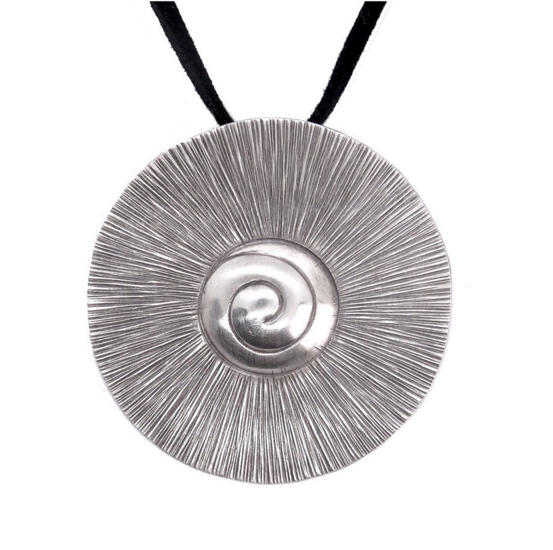 May include: A silver pendant necklace with a circular design featuring a spiral in the centre. The pendant is attached to a black cord.