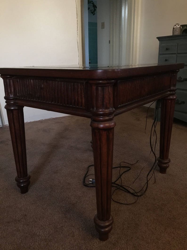 Op de afbeelding: Een donkerbruine houten bijzettafel met een glazen blad en gedraaide poten. De tafel staat op een bruin tapijt.