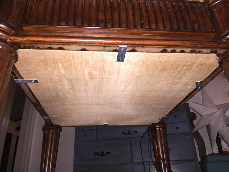 Op de afbeelding: De onderkant van een houten tafel met een bevestigd multiplexpaneel. Het paneel is bevestigd met metalen beugels. De tafel heeft een donkerbruine afwerking.
