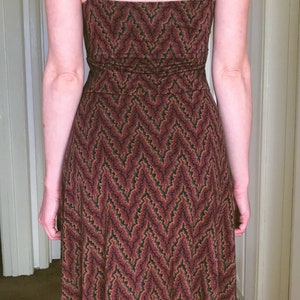 Puede incluir: Vestido sin mangas con estampado de chevr&oacute;n en tonos burdeos, negro y verde. El vestido tiene un escote cuadrado y tirantes anchos. La tela parece ser de punto suave y el vestido llega a la mitad de la pantorrilla.