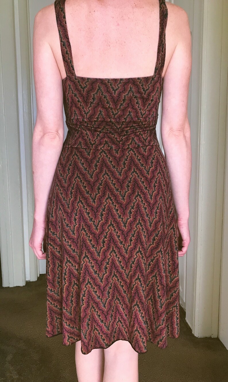 Puede incluir: Vestido sin mangas con estampado de chevr&oacute;n en tonos burdeos, negro y verde. El vestido tiene un escote cuadrado y tirantes anchos. La tela parece ser de punto suave y el vestido llega a la mitad de la pantorrilla.