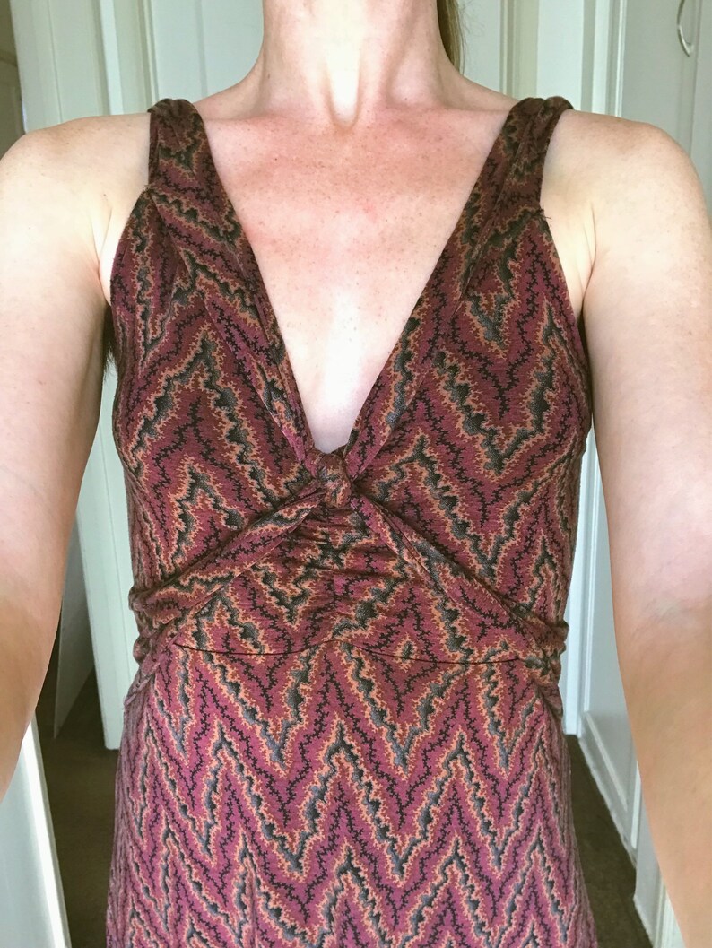 Puede incluir: Vestido sin mangas con escote en V y detalle anudado en el busto. El vestido presenta un estampado de zigzag burdeos, negro y beige. El vestido tiene un corpi&ntilde;o ajustado y una falda fluida.