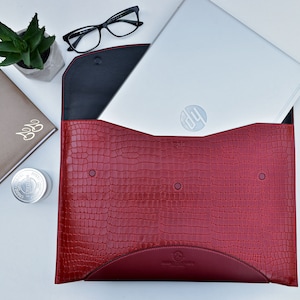 May include: Red leather laptop sleeve with a crocodile pattern. The sleeve is open and a silver laptop with the HP logo is inside.