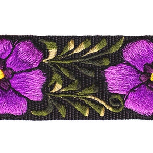 以下が含まれることがあります： 黒いリボンに紫色の刺繍の花と緑の葉が描かれています。花の中心は黄色です。