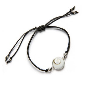 Può includere: Un braccialetto con cordino nero con un design a spirale bianco e beige incastonato in una lunetta color argento. Il braccialetto ha nodi scorrevoli regolabili e piccole perline color argento. Lo sfondo è bianco.