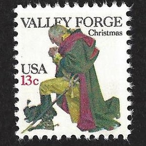 May include: A postage stamp featuring a kneeling figure in a green coat and red scarf, with the text "VALLEY FORGE Christmas" and "USA 13c". The stamp has a white background with a perforated edge.