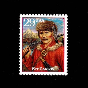 May include: A vintage 29 cent US postage stamp featuring a portrait of Kit Carson, a famous American frontiersman. The stamp depicts Carson in a fur hat and coat, holding a rifle and a knife. The background is a colorful landscape with mountains and a river.