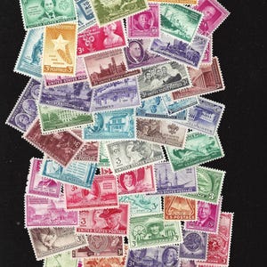 May include: A collection of vintage United States postage stamps, featuring a variety of designs and colors. The stamps depict historical figures, landmarks, and events, including the American Red Cross, the U.S. Coast Guard, and the National Capital Sesquicentennial.