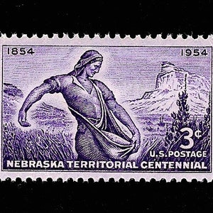 May include: A purple 3-cent U.S. postage stamp commemorating the Nebraska Territorial Centennial. The stamp features a man in a long-sleeved shirt and pants, holding a sack of grain. The stamp also features a mountain in the background. The text "1854" and "1954" are printed on the stamp.
