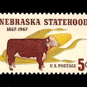 May include: A vintage 5-cent US postage stamp commemorating the 100th anniversary of Nebraska statehood. The stamp features a brown and white cow standing in front of a yellow ear of corn.