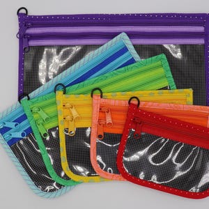 May include: A collection of colorful zippered pouches in various sizes. The pouches feature a clear window, a black zipper, and a black ring. The colors include purple, blue, green, yellow, orange, and red. The pouches are made of fabric.