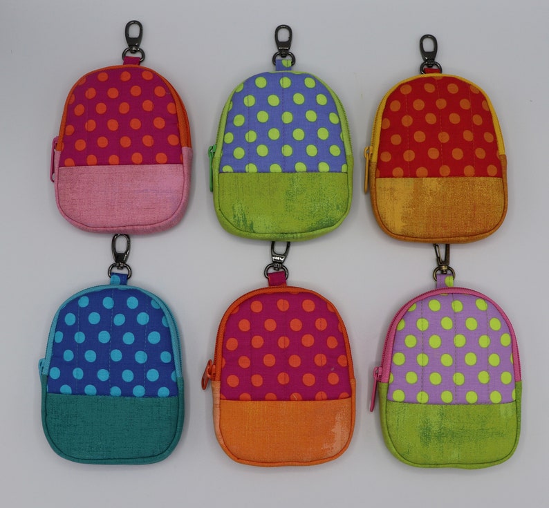 May include: Six small, colorful, polka dot fabric bags with a zipper closure and a loop for attaching a key chain. The bags are in various colors, including pink, green, blue, orange, and purple.