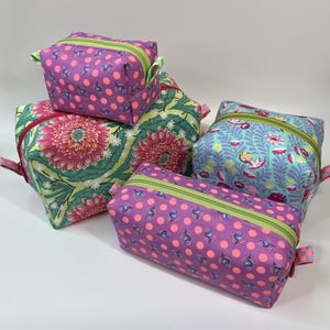 May include: A collection of four fabric pouches in various sizes. Two pouches feature a purple background with pink polka dots and small blue thistle motifs, while the others display a vibrant floral pattern with pink flowers on a teal background.