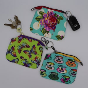 Puede incluir: Tres pequeñas bolsas con cremallera con diferentes patrones. La primera bolsa es verde con un patrón de mariposa. La segunda bolsa es turquesa con un patrón de rosa. La tercera bolsa es turquesa con un patrón de taza de té.