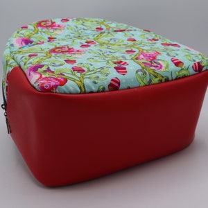 Puede incluir: Una mochila de tela con estampado rojo y azul con una base de cuero rojo. La mochila tiene una cremallera y un asa superior.