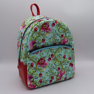 Puede incluir: Una mochila azul y roja con un estampado floral con ardillas rosas y bellotas. La mochila tiene un bolsillo con cremallera en la parte delantera.