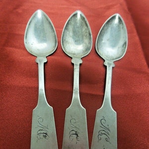 May include: Three silver spoons with ornate handles. Each spoon has the inscription "M.E." on the back.