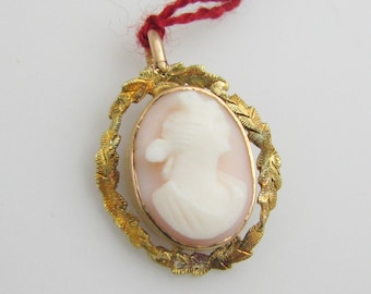 May include: A gold cameo pendant with a white cameo of a woman's profile in a gold leaf frame.