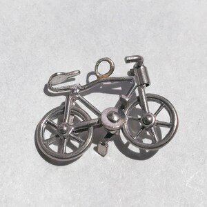 May include: A silver charm in the shape of a bicycle. The charm has a loop at the top for attaching to a bracelet or necklace.
